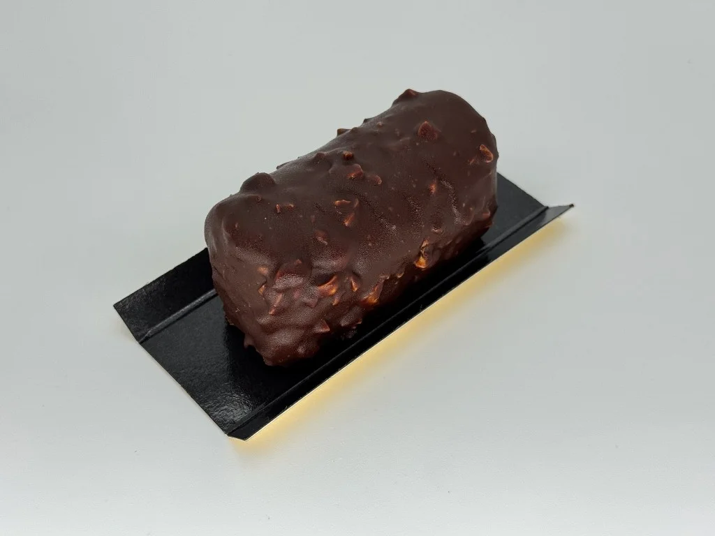 Brownie–chocolate dessert - Peanut brownie layered with silky caramel, wrapped in airy chocolate mousse, and finished with a dark chocolate glaze studded with crunchy nuts.